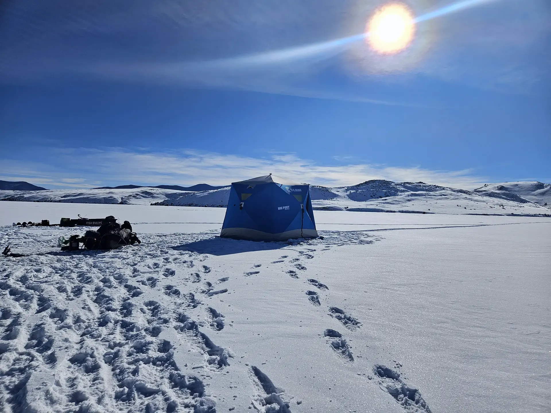 A thermal ice fishing shelter on the frozen reservoir under a low winter sun