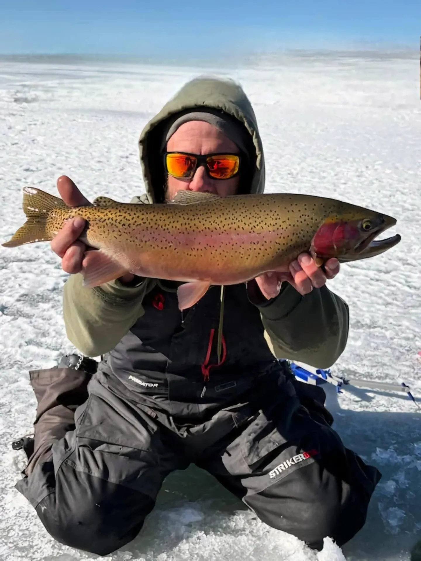 A kneeling angler holding a heavy rainbow trout across both hands