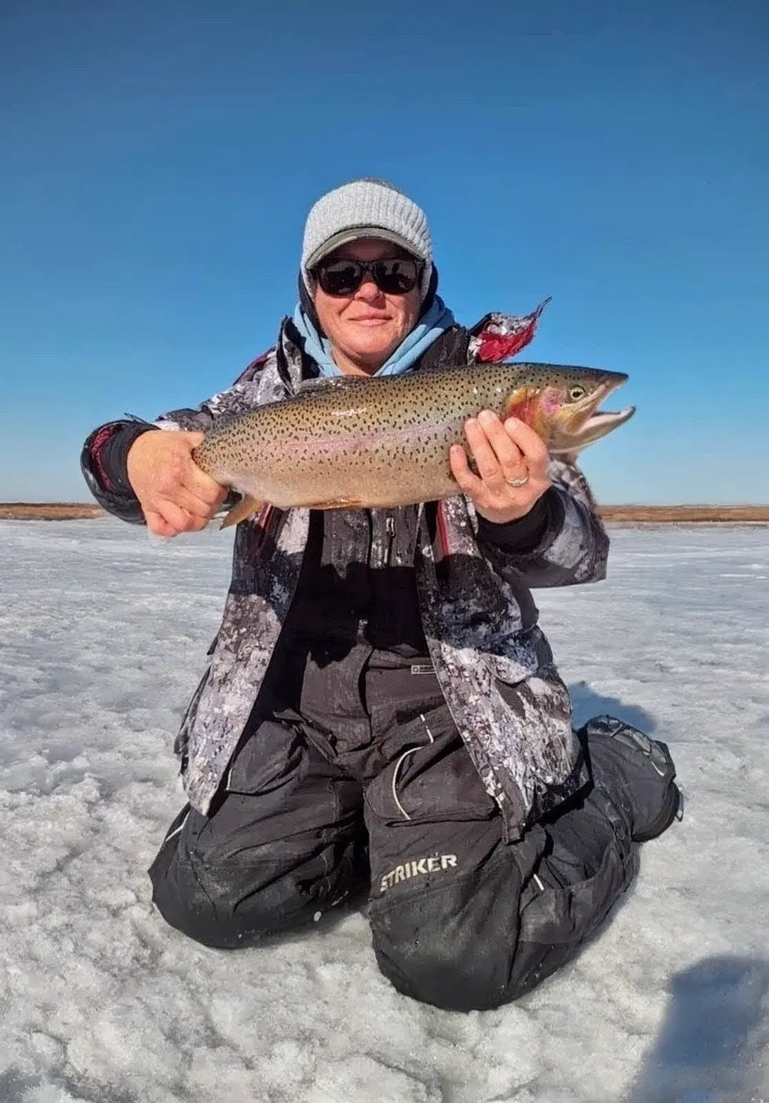 Leslie Branin kneeling on the ice at Eleven Mile Reservoir holding a large trout