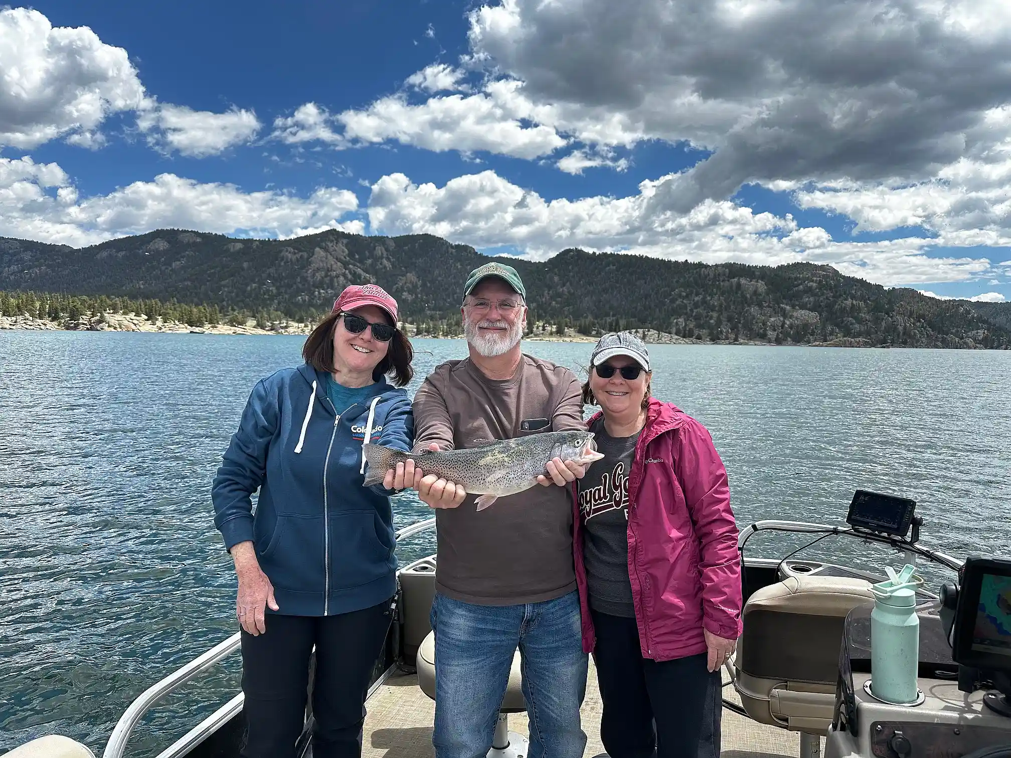 Two women and a man holding a rainbow trout aboard the pontoon on Eleven Mile Reservoir