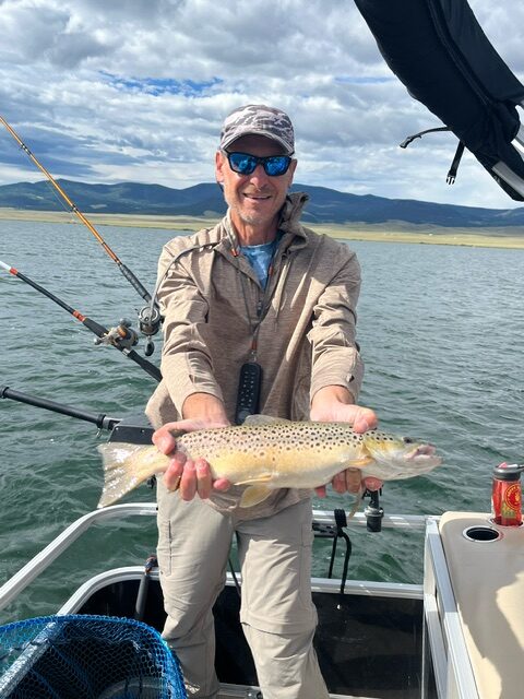Jeff Kaplan holding a brown trout aboard the pontoon, Eleven Mile Reservoir behind him
